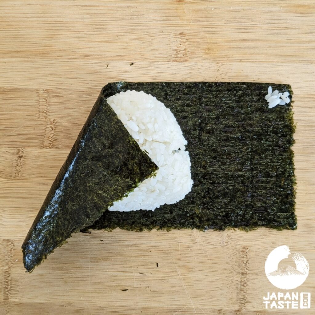 Fold the left side over the onigiri and add some rice in the right corner of the nori